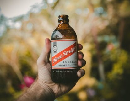 Bottle of red stripe beer held in a man's hand as one of Jamaica's favourite dishes
